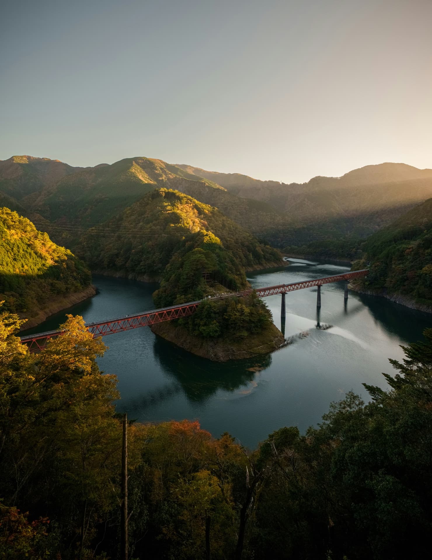 Train crossing a bridge over a Japanese mountain lake at golden hour